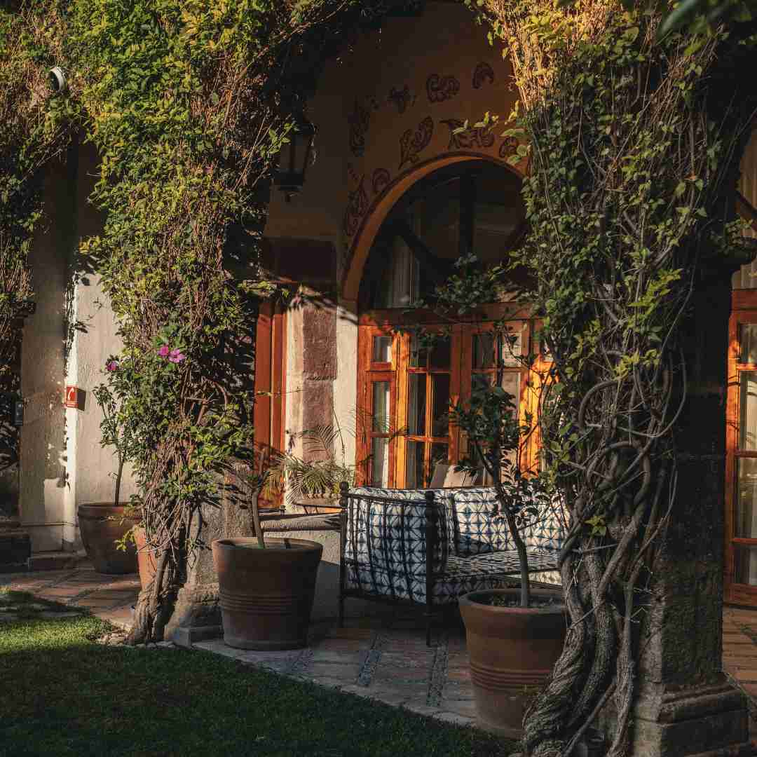 A welcoming photograph capturing the porch of the Deluxe Suite at Belmond Casa de Sierra Nevada in San Miguel de Allende, Mexico. Rustic yet elegant furnishings and lush gardens create a private haven with colonial authenticity.