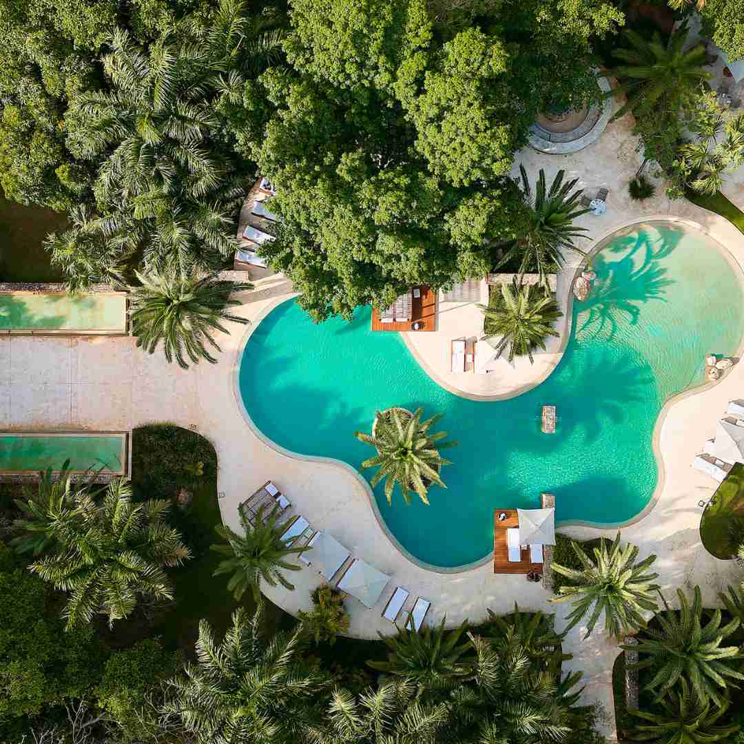 A captivating aerial view of the pool at Chablé Spa & Resort. The geometric design of the pool reflects against lush greenery and the expansive resort landscape.