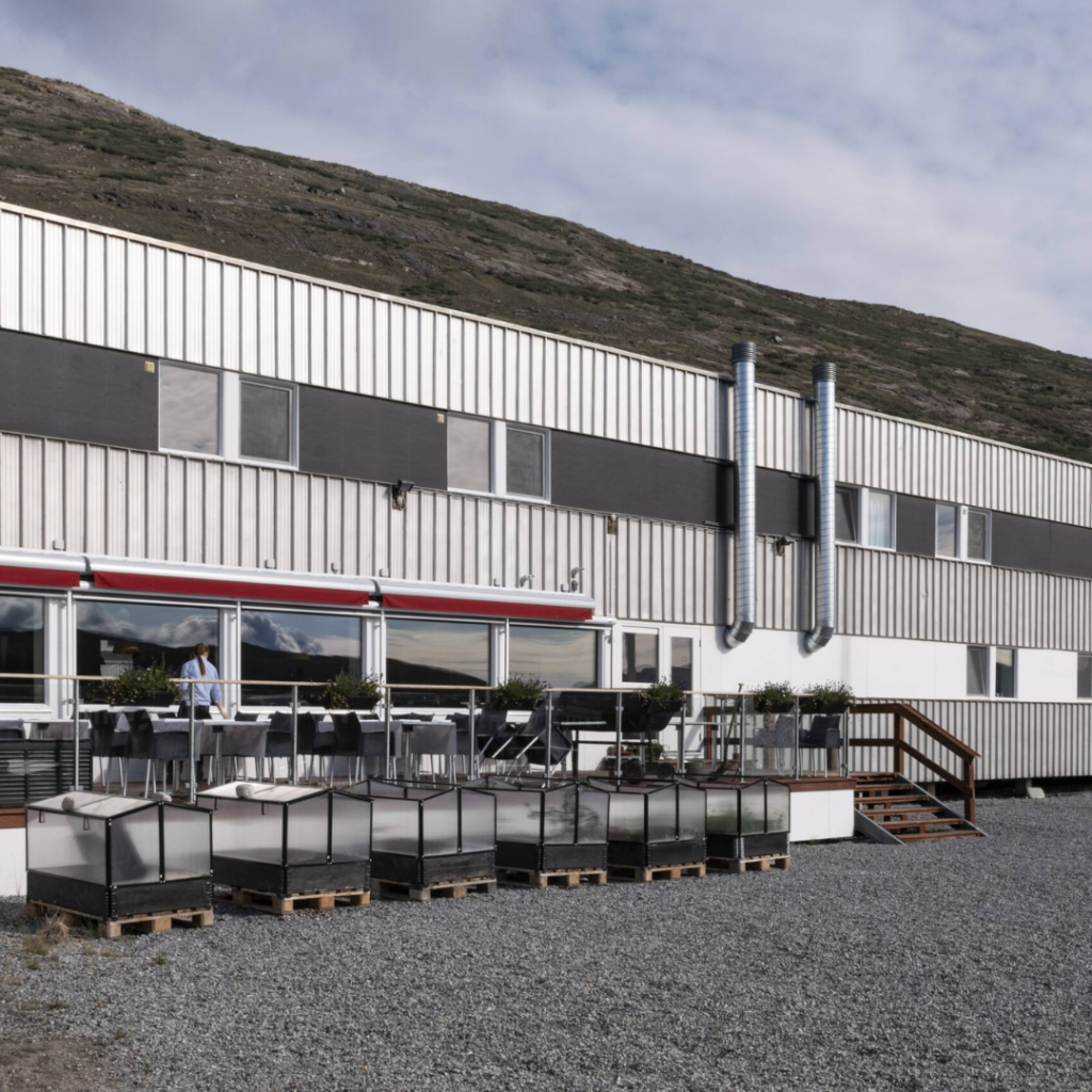 A view of Hotel Kangerlussuaq in Kangerlussuaq, Greenland, showcasing its industrial building and inviting restaurant. The architectural blend of functionality and comfort is evident in this Arctic setting, providing a unique and cozy atmosphere for guests in the heart of Greenland's wilderness.
