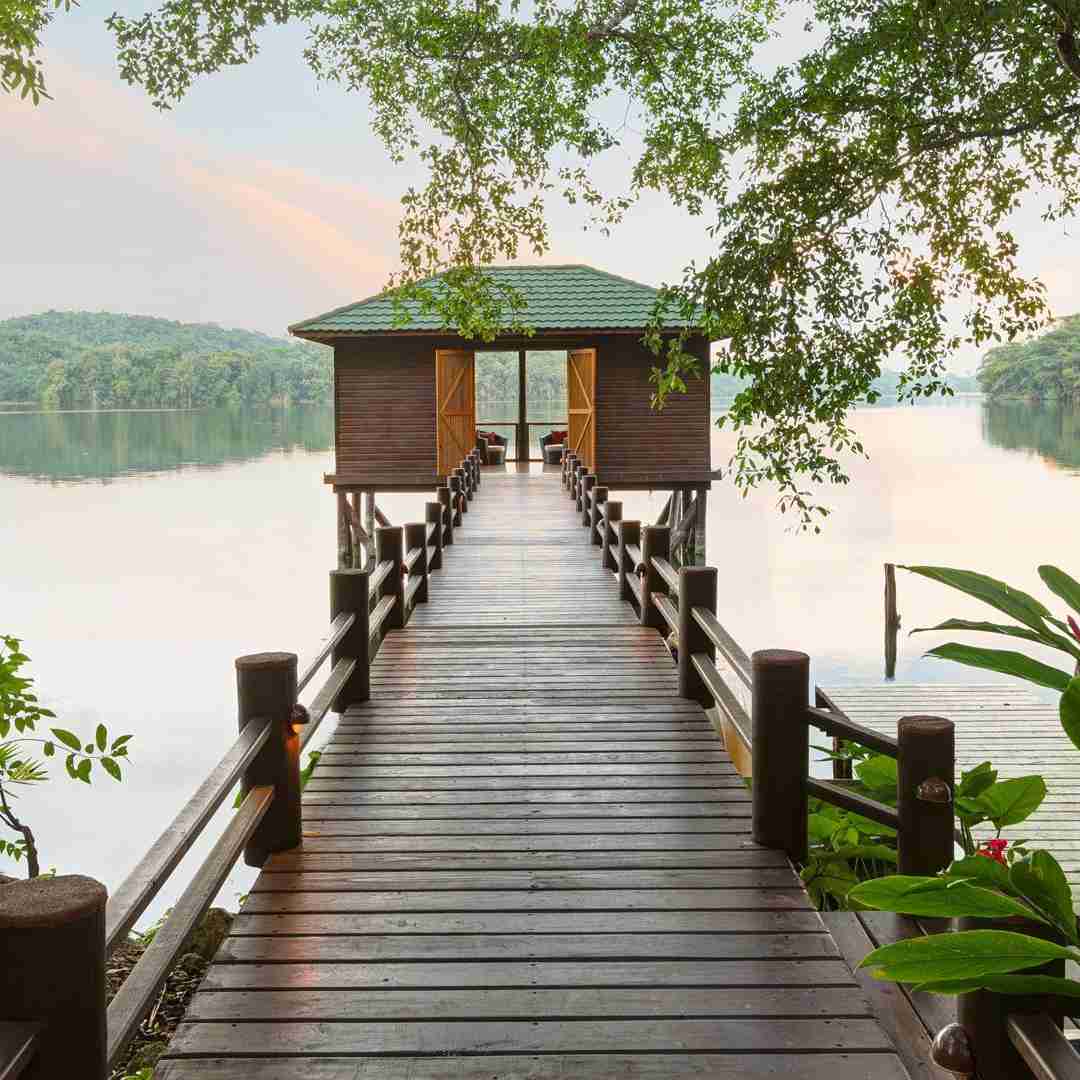 Serene scene at Las Lagunas Boutique Hotel in Flores, Peten, Guatemala. A picturesque dock surrounded with lush greenery leads to a charming gazebo at its end. Beyond, a breathtaking landscape unfolds, showcasing a tranquil lake framed by majestic mountains. A perfect blend of natural beauty and luxurious retreat in the heart of Guatemala