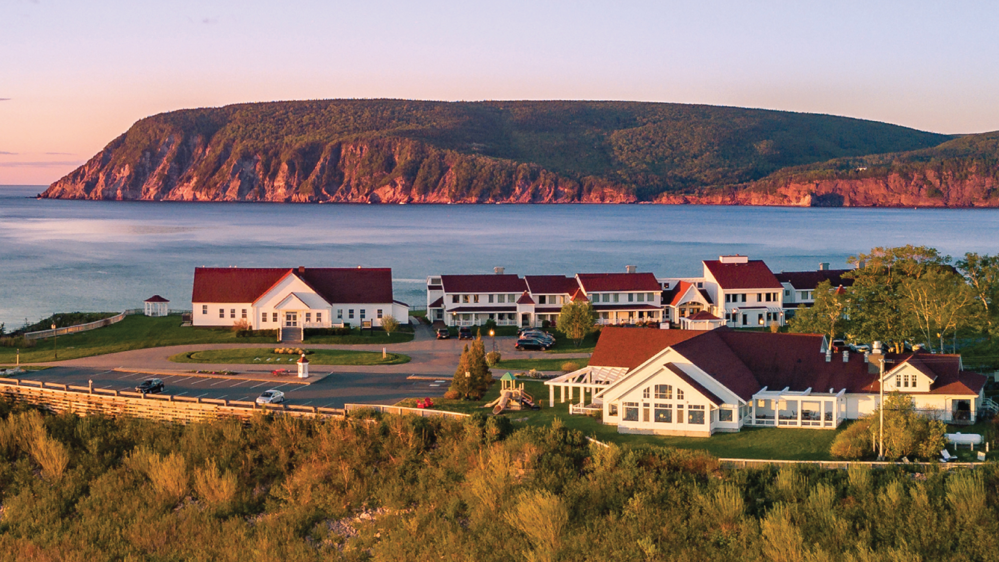 A stunning aerial view of the Keltic Lodge hotel nestled amidst the breathtaking landscapes of Cape Breton Island, with the vast Atlantic Ocean stretching beyond. Tailored for self-flying pilots