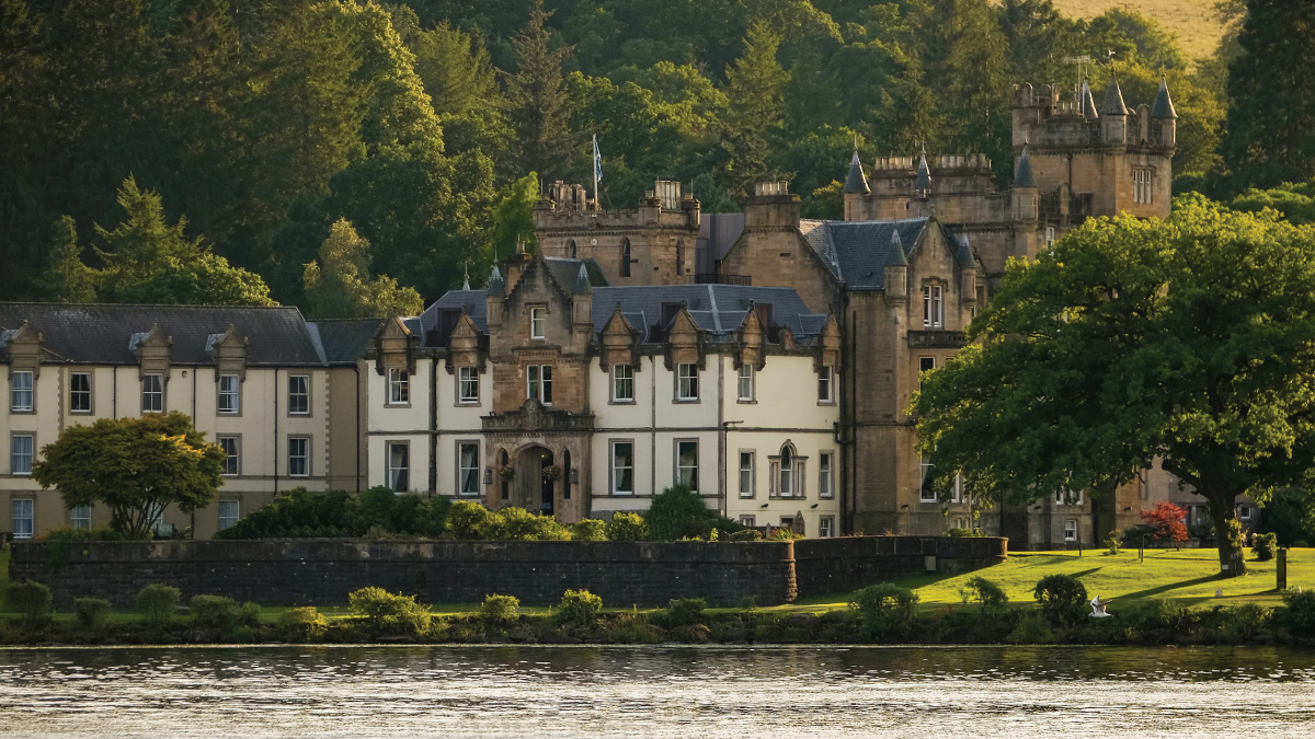 An enchanting view of Cameron House Castle standing proudly on the shores of Loch Lomond, Scotland, surrounded by verdant hills and serene waters. Offering inspiration for a journey to Europe for self-flying pilots