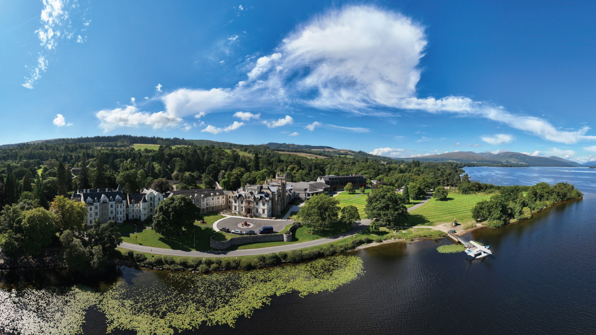 A captivating aerial view of Cameron House nestled on the banks of Loch Lomond, Scotland, surrounded by lush greenery and tranquil waters. Promoting a journey to Europe for self-flying pilots with their own TBM aircraft