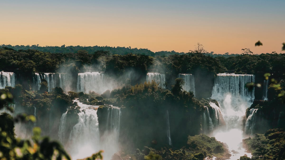A mesmerizing aerial view of the sunset at Iguazu Falls, Argentina, casting a golden glow over the cascading waters amidst the lush greenery. A captivating destination for self-flying pilots exploring South America.