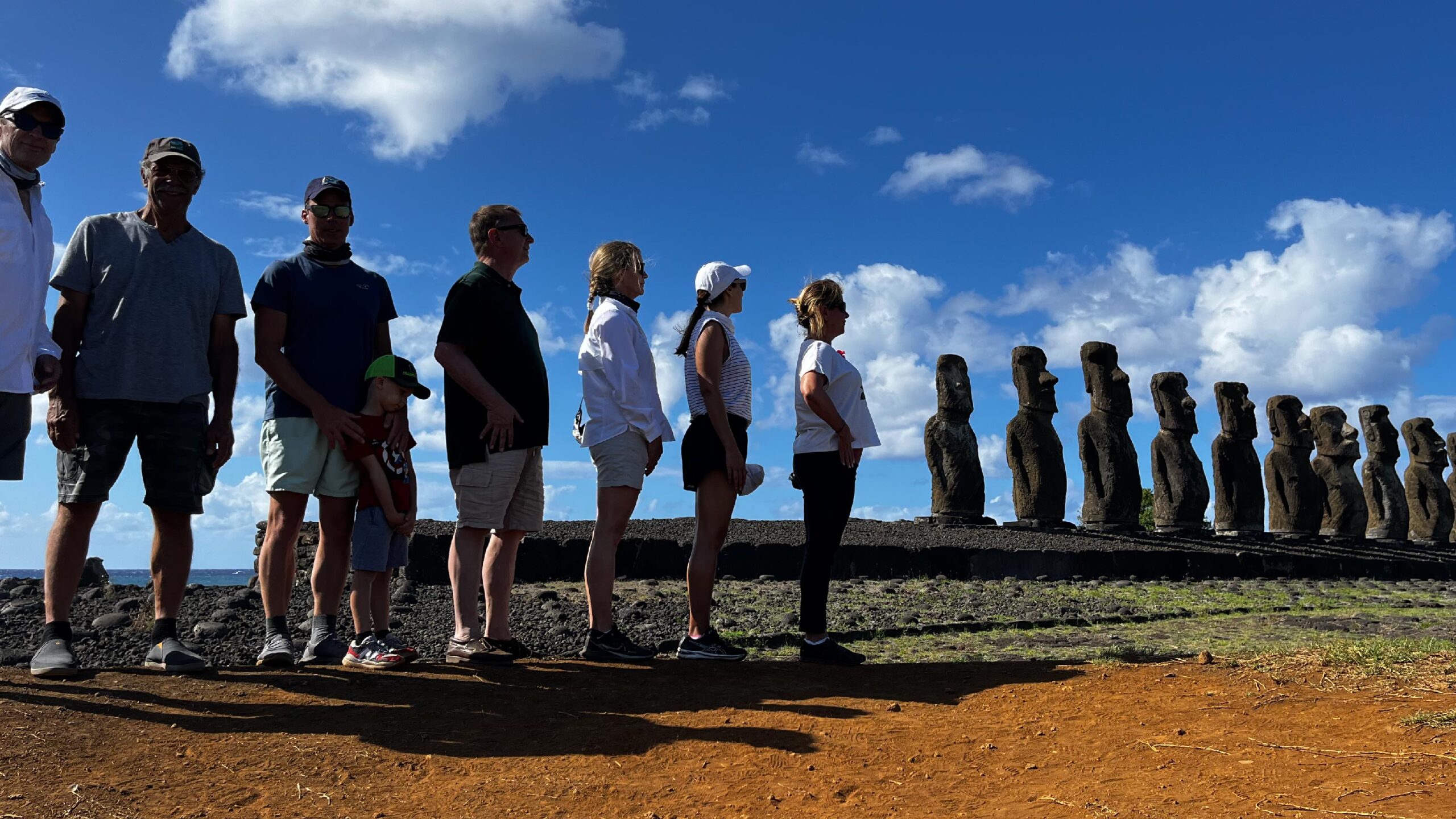 Moai statues on Easter Island, Chile. The statue, carved from stone, stands tall against a backdrop of lush green grass and a partly cloudy sky.