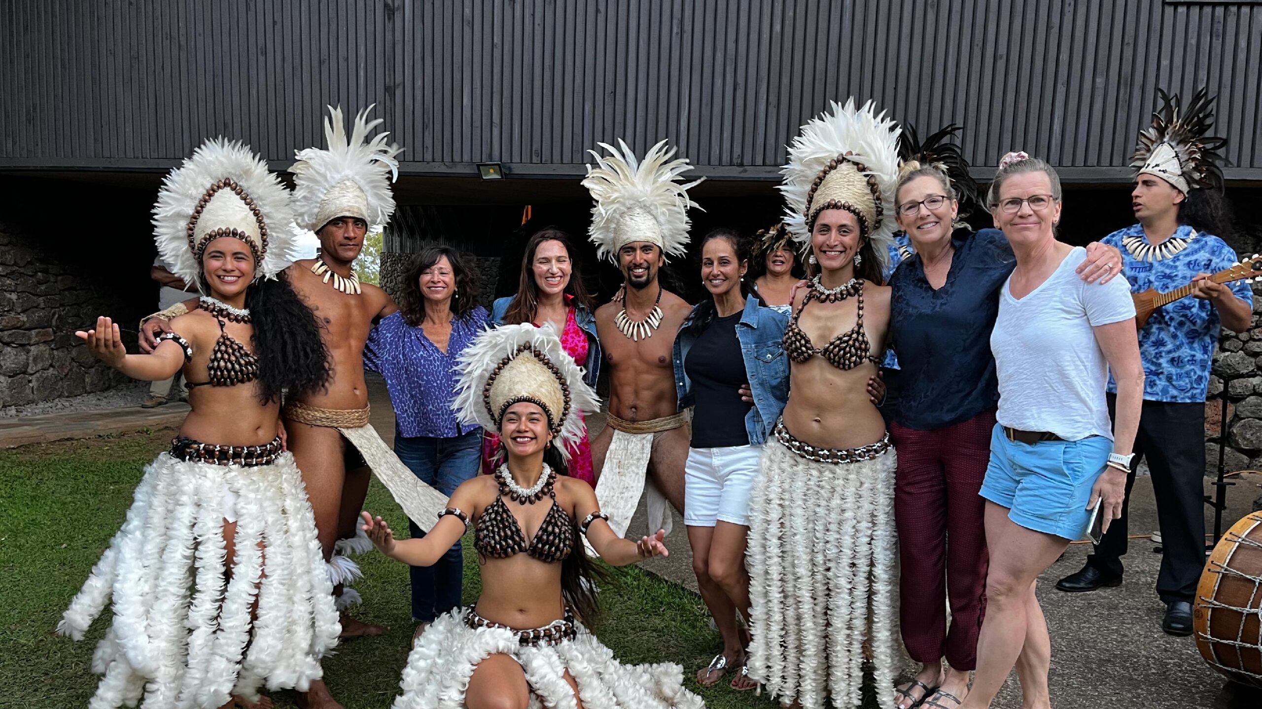 A group of travelers poses with members of the Rapa Nui people on Easter Island, Chile. The Rapa Nui people are dressed in traditional clothing, including feathered headdresses and decorative accessories. The travelers and the Rapa Nui people stand together smiling