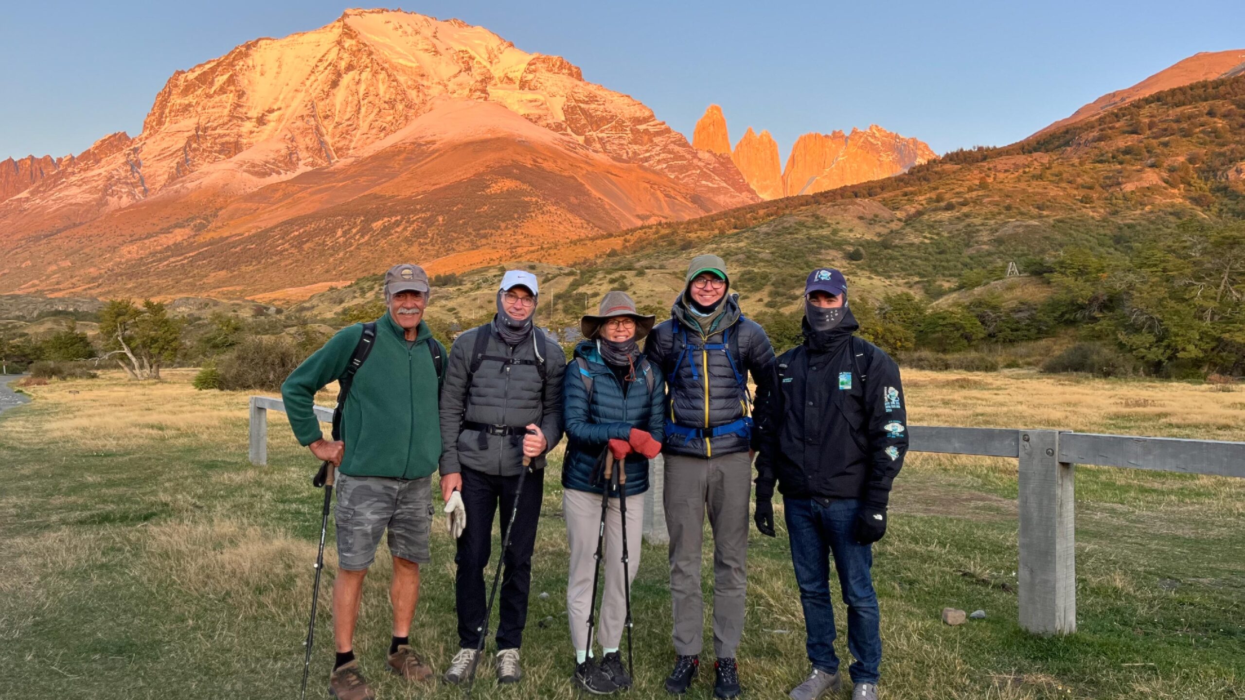 A group of travelers is trekking through Torres del Paine in Patagonia, Chile. They hike along a rugged trail, surrounded by breathtaking scenery that includes towering granite peaks, lush green valleys, and glacial rivers.