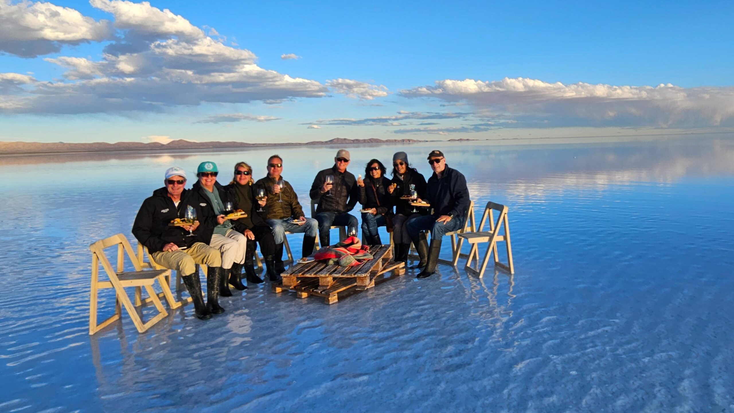 A group of travelers eating lunch on the reflective salt flats of Salar de Uyuni, Bolivia, under a bright blue sky.