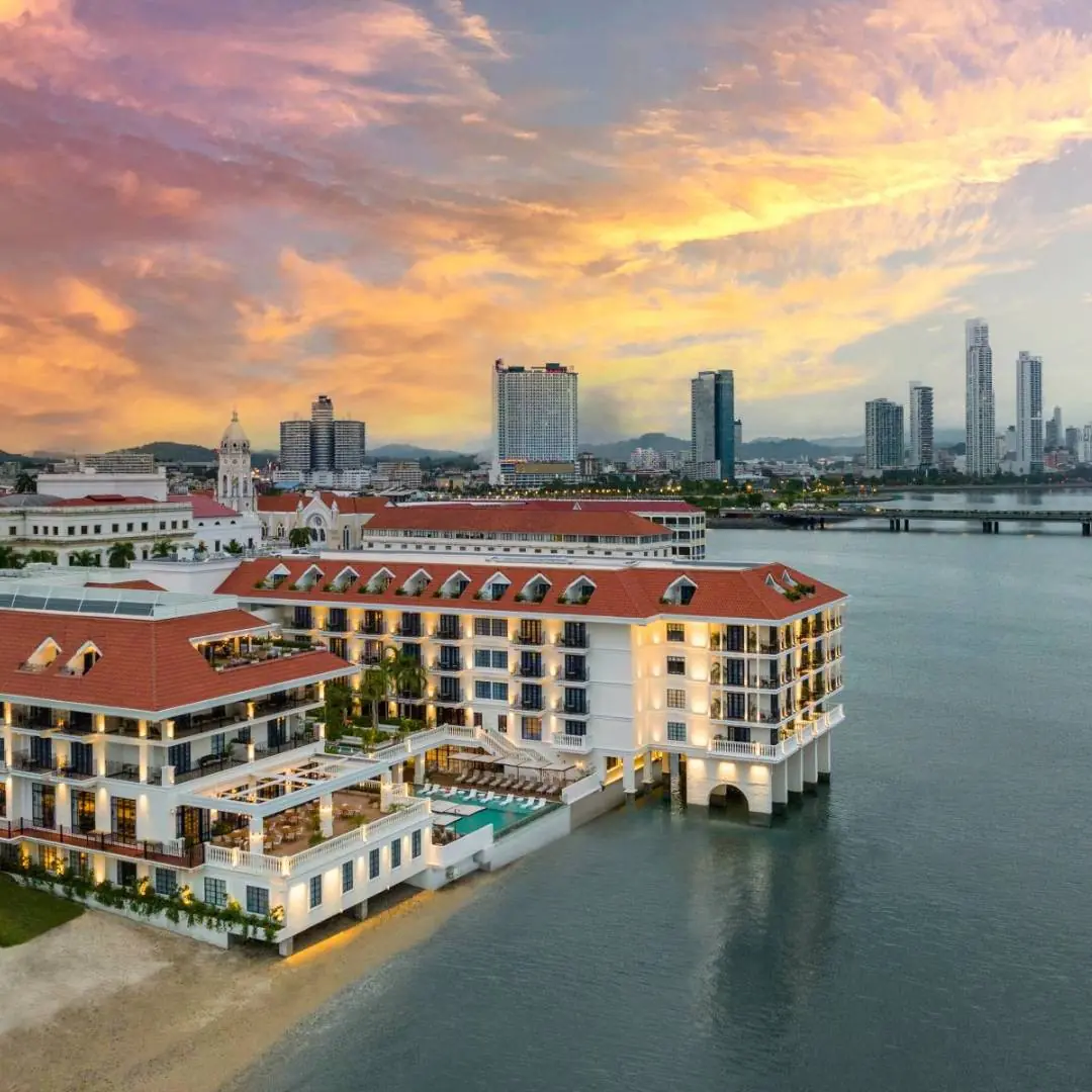 A photograph showcasing the historic elegance of Sofitel Legend Casco Viejo in Panama City. The hotel's facade, rich in architectural details, stands proudly against a clear blue sky. The image highlights a charming courtyard, with cobblestone pathways and lush greenery, creating an inviting atmosphere.